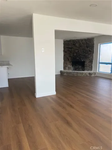 an empty room with wooden floor fireplace and windows