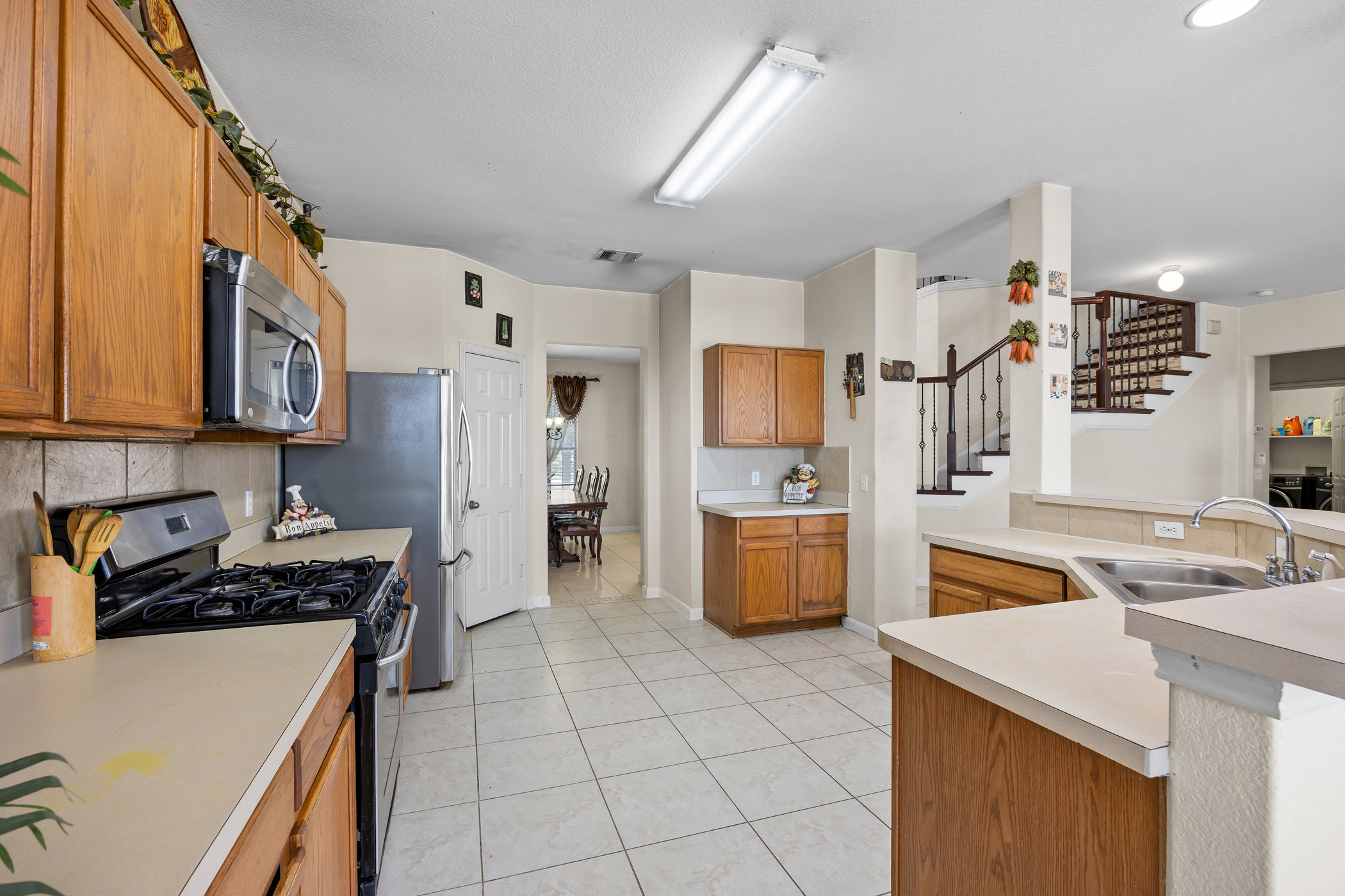 3502 Shiraz Loop Round Rock, TX 78665 - Photo 4 of 23 Kitchen with stainless steel appliances, wood finish cabinetry, light countertops, backsplash, and light tile patterned flooring