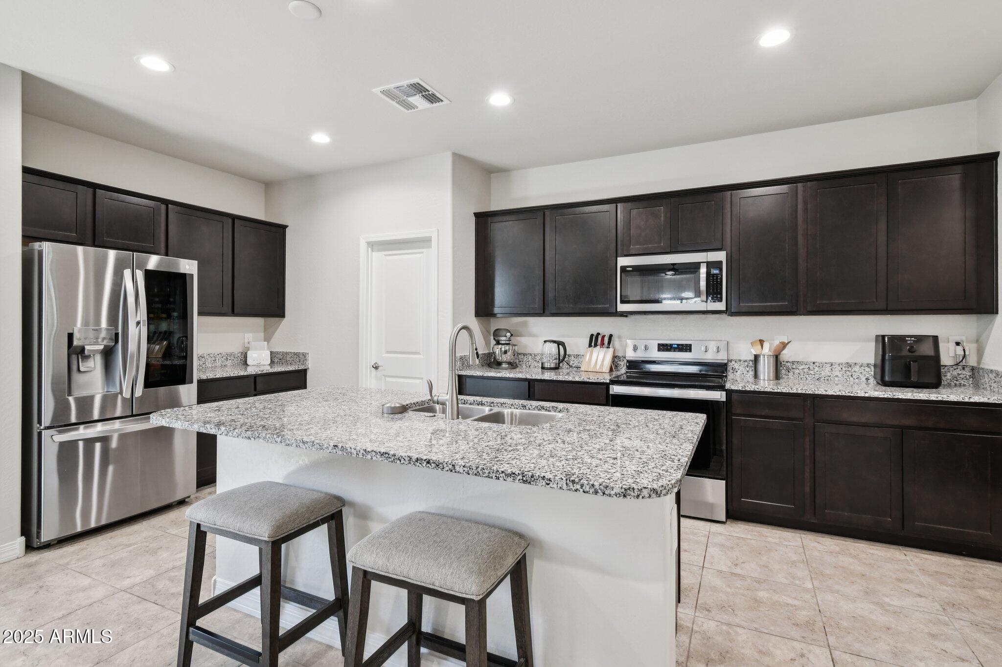 18819 West Farmer Road Buckeye, AZ 85326 - Photo 3 of 23 a kitchen with granite countertop a refrigerator and a stove top oven