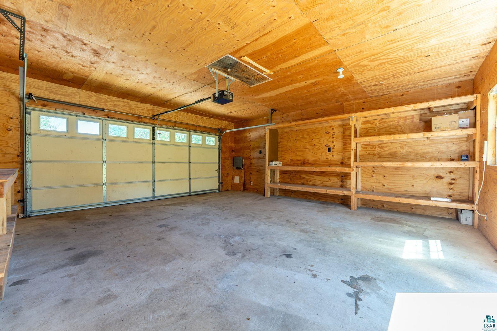 9734 Alango Road Angora, MN 55703 - Photo 20 of 41 Spacious garage featuring a concrete floor, built-in wooden shelving, and a large garage door with transom windows