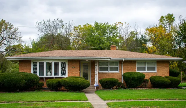 a view of a brick house with a yard plants and large trees