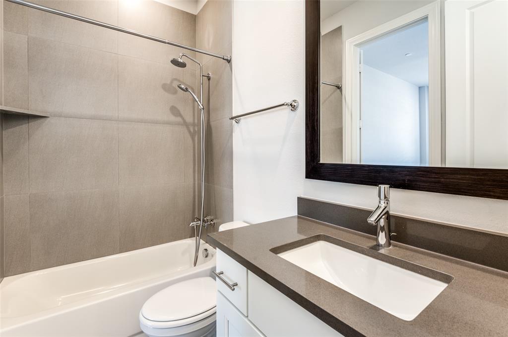 5421 Patterson Street Irving, TX 75039 - Photo 13 of 32 Bathroom featuring a white bathtub, gray tile shower surround with integrated shelf, and a shower head with an additional handheld sprayer
