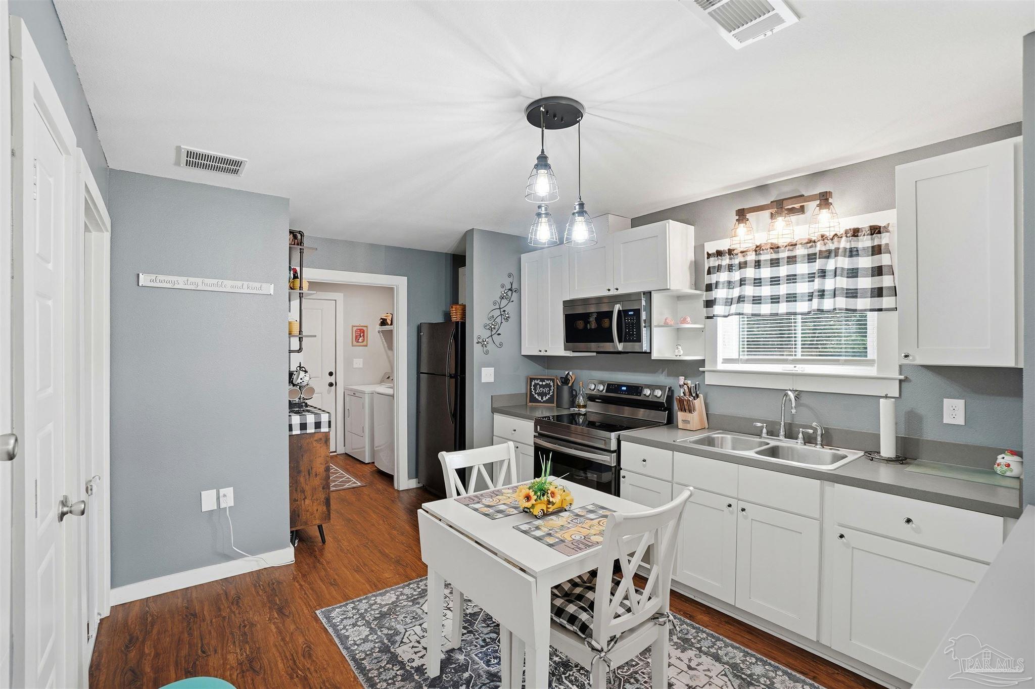 402 Front Street Century, FL 32535 - Photo 9 of 48 a kitchen with stainless steel appliances a refrigerator a stove a sink dishwasher and white cabinets with wooden floor