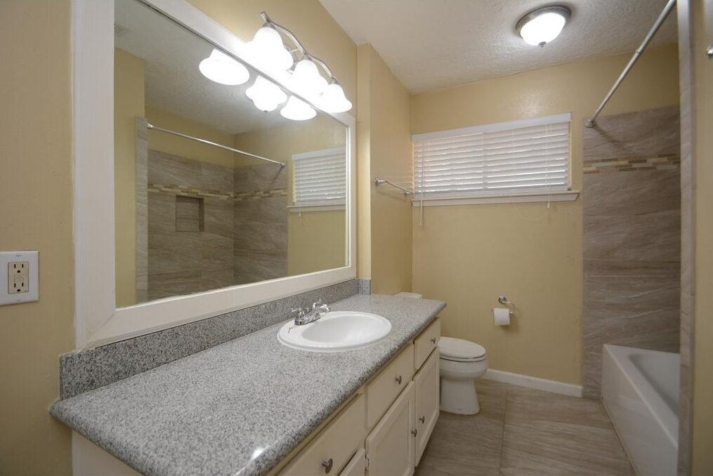 15 South Tallowberry Drive Spring, TX 77381 - Photo 21 of 26 Bathroom with granite countertop vanity, ample storage, large mirror, bathtub with tile surround, and natural light from a window.