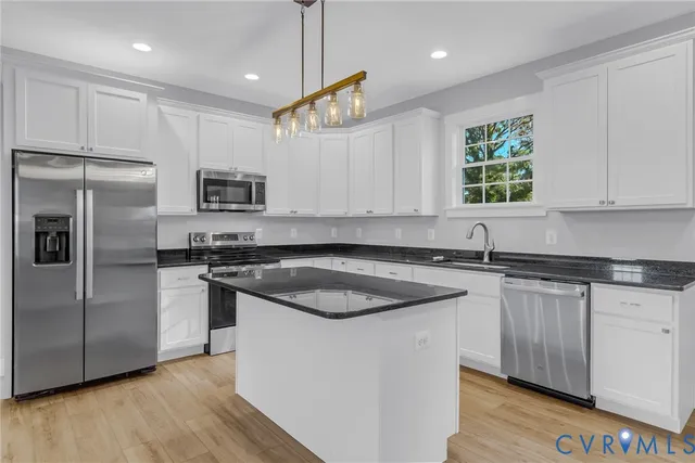 a kitchen with stainless steel appliances granite countertop a sink a stove a refrigerator and island with wooden floor