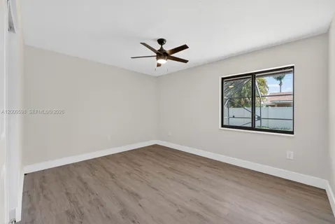 an empty room with wooden floor ceiling fan and window