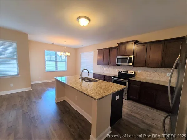 a kitchen with stainless steel appliances granite countertop wooden cabinets a sink dishwasher a stove and a refrigerator with wooden floor