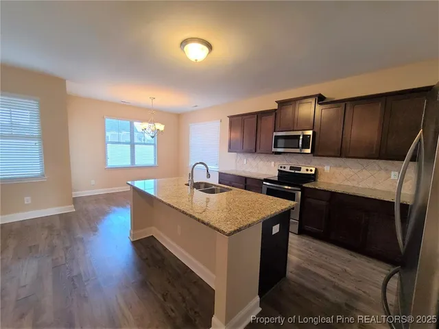 a kitchen with stainless steel appliances granite countertop wooden cabinets a sink dishwasher a stove and a refrigerator with wooden floor