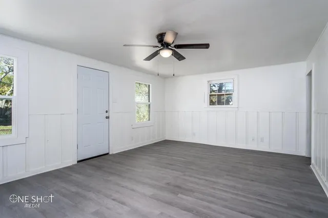 an empty room with wooden floor ceiling fan and windows