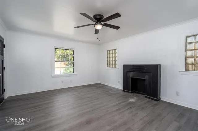 an empty room with windows a fireplace a ceiling fan and wooden floor