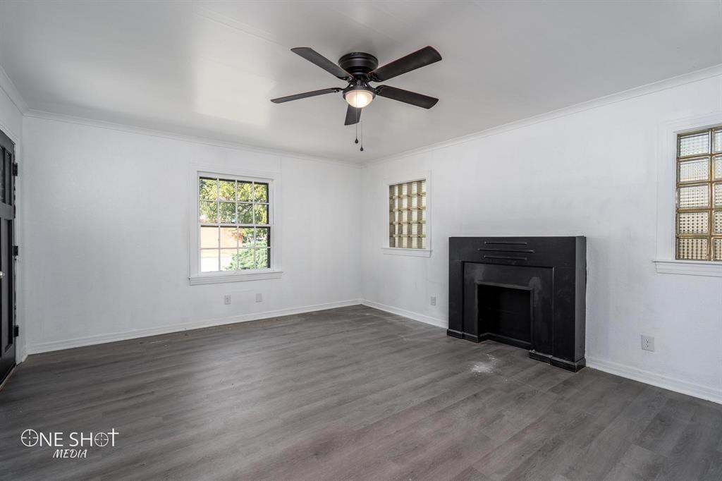 1909 Highland Avenue Abilene, TX 79605 - Photo 2 of 23 an empty room with windows a fireplace a ceiling fan and wooden floor