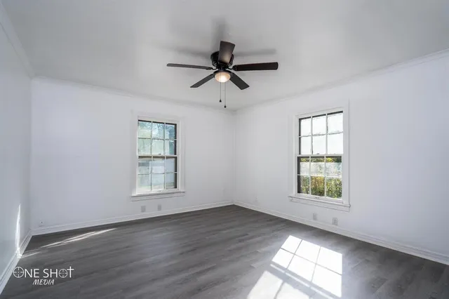 an empty room with wooden floor ceiling fan and windows