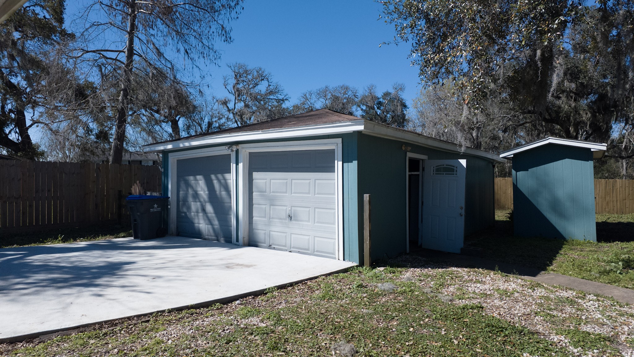 407 Tamarind Street Lake Jackson, TX 77566 - Photo 4 of 36 This photo features a detached two-car garage with blue siding and white trim, situated in a spacious backyard.