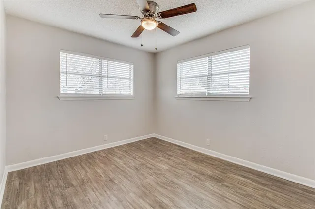 an empty room with wooden floor chandelier fan and windows