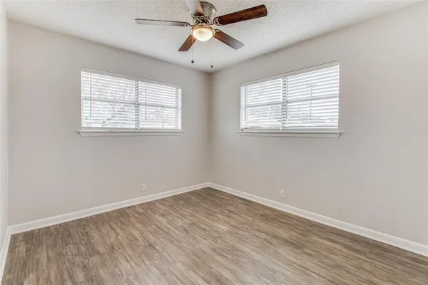 an empty room with wooden floor chandelier fan and windows