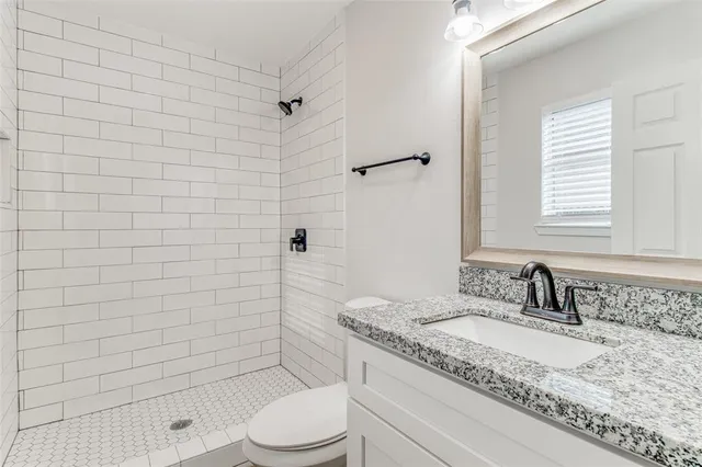 a bathroom with a granite countertop toilet a sink a mirror and shower