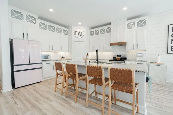 a kitchen with stainless steel appliances kitchen island granite countertop a refrigerator a stove a sink and white cabinets with wooden floor