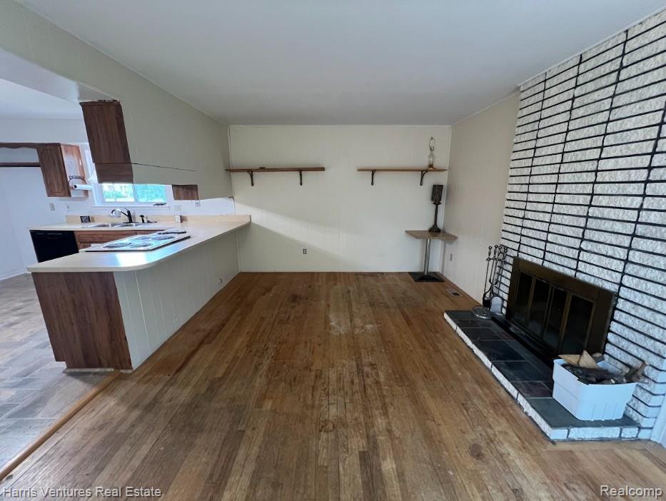 28482 Sutherland Avenue Warren, MI 48088 - Photo 11 of 25 Spacious family room featuring wood-finish flooring, a prominent brick fireplace with a black tile hearth, and ceiling-mounted light fixtures