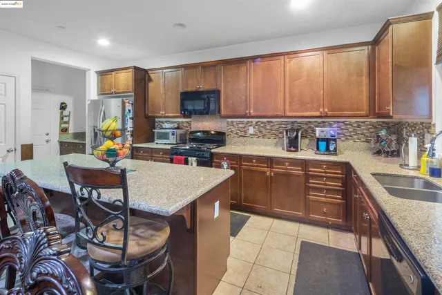 a kitchen with stainless steel appliances kitchen island granite countertop a sink a stove a refrigerator cabinets and chairs