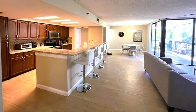 a living room with stainless steel appliances kitchen island granite countertop a refrigerator a sink dishwasher a dining table and chairs with wooden floor