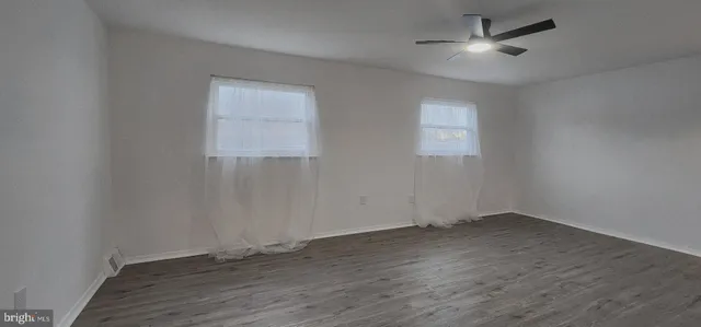 an empty room with wooden floor ceiling fan and windows