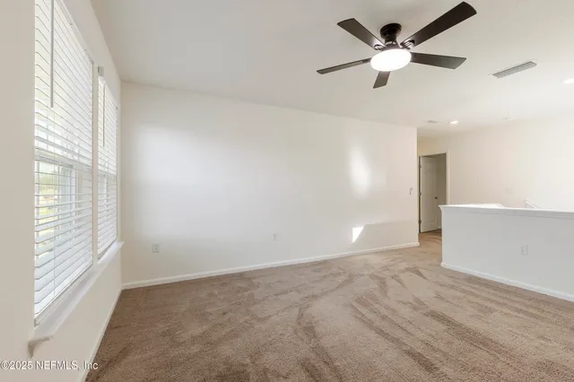 a view of an empty room with window and a ceiling fan