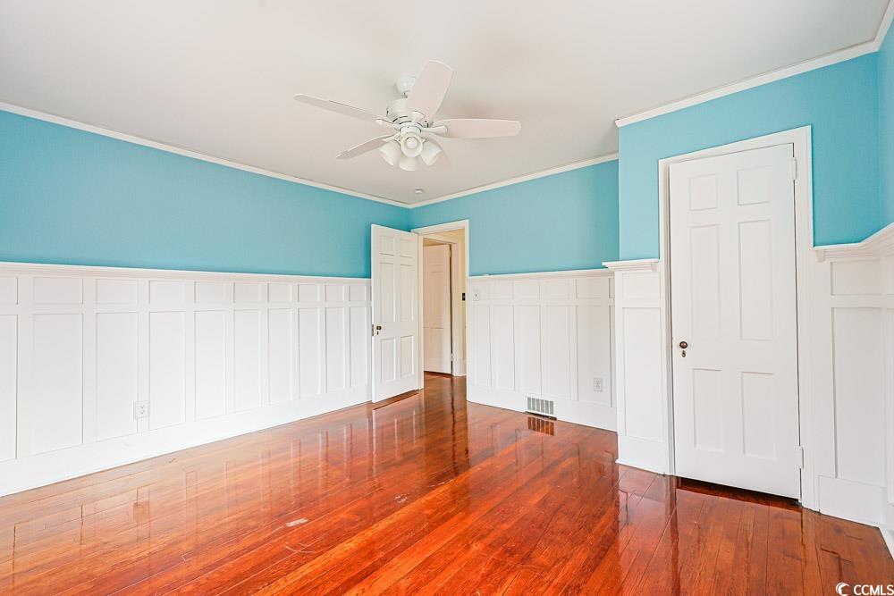 509 Beaty Street Conway, SC 29526 - Photo 21 of 40 Unfurnished bedroom featuring a wainscoted wall, ornamental molding, a ceiling fan, dark wood-type flooring, and a decorative wall