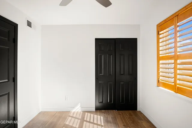 an empty room with wooden floor chandelier fan and windows