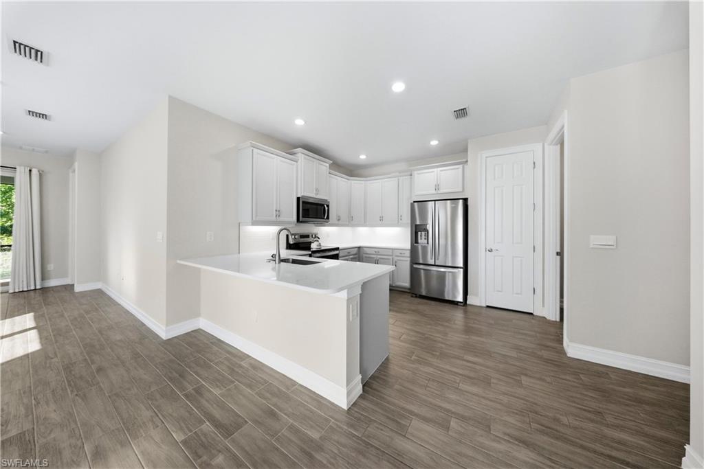 1059 Enbrook Loop Naples, FL 34114 - Photo 7 of 40 Kitchen with stainless steel appliances, white cabinetry, wood tiled floors, a peninsula, and recessed lighting
