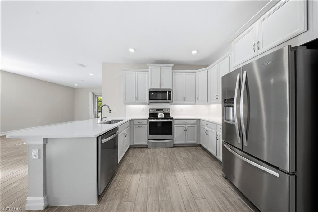 1059 Enbrook Loop Naples, FL 34114 - Photo 8 of 40 Kitchen featuring stainless steel appliances, a peninsula, light wood-style flooring, tasteful backsplash, and recessed lighting