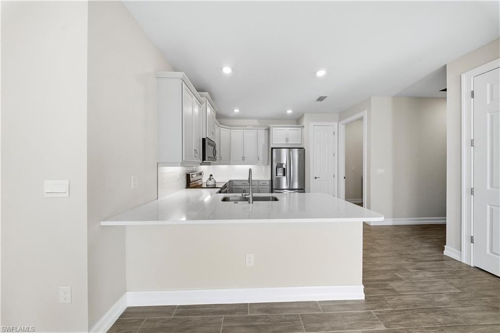 1059 Enbrook Loop Naples, FL 34114 - Photo 9 of 40 Kitchen featuring white cabinets, stainless steel appliances, a peninsula, wood tiled floors, and light stone countertops