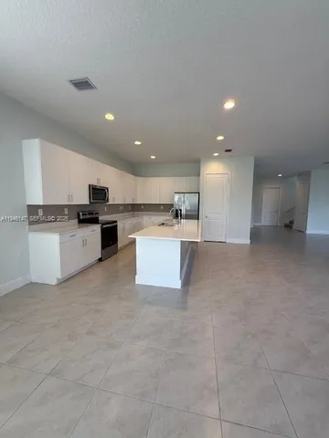 a large white kitchen with kitchen island a stove a sink a refrigerator and white cabinets