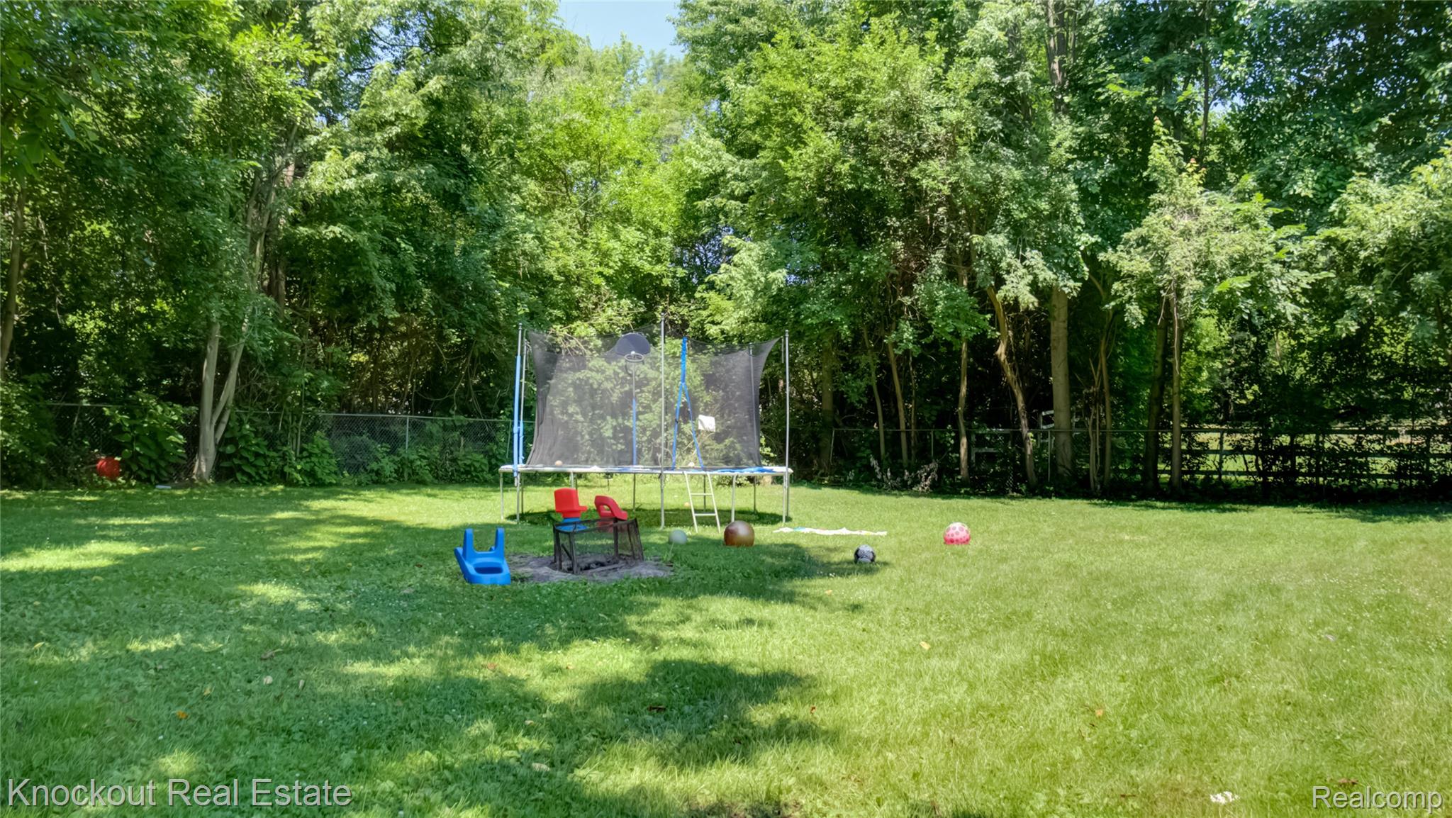 4195 Williamson Road Saginaw, MI 48601 - Photo 44 of 50 Expansive grassy yard area with a chain-link fence and mature trees providing natural screening