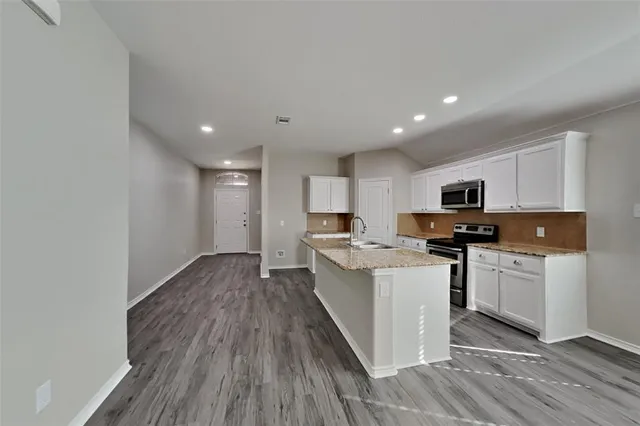 a kitchen with stainless steel appliances granite countertop a stove top oven a sink a refrigerator with white cabinets and wooden floor