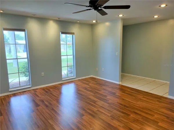 an empty room with wooden floor fan and windows