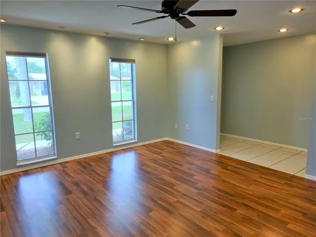 an empty room with wooden floor fan and windows