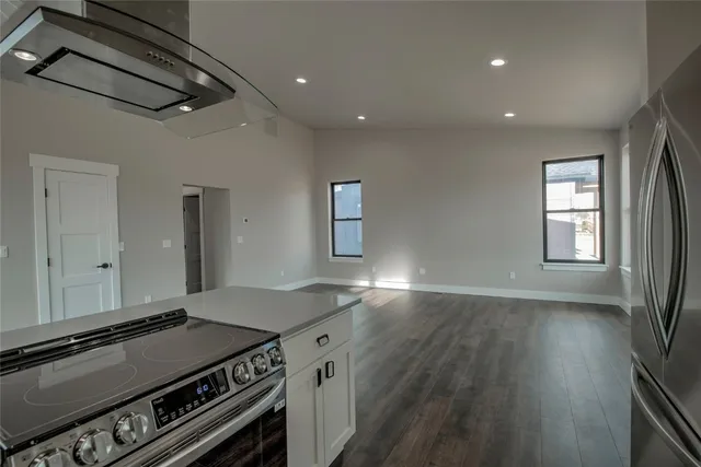 a open kitchen with stainless steel appliances a stove a chimney a sink and wooden floor