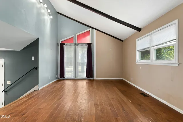 a view of an empty room with wooden floor and a window