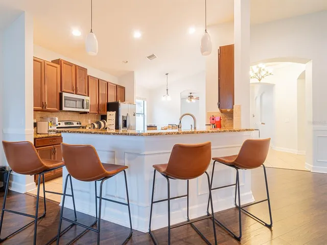 a kitchen with stainless steel appliances kitchen island granite countertop a dining table chairs and a sink