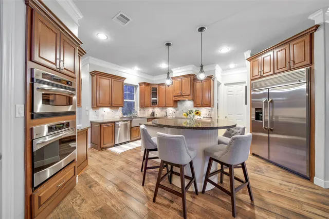 a kitchen with stainless steel appliances kitchen island granite countertop a refrigerator a stove a oven and white cabinets with wooden floors