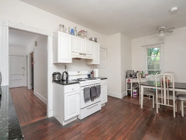 a kitchen with stainless steel appliances a white stove top oven a dining table and chairs with wooden floor