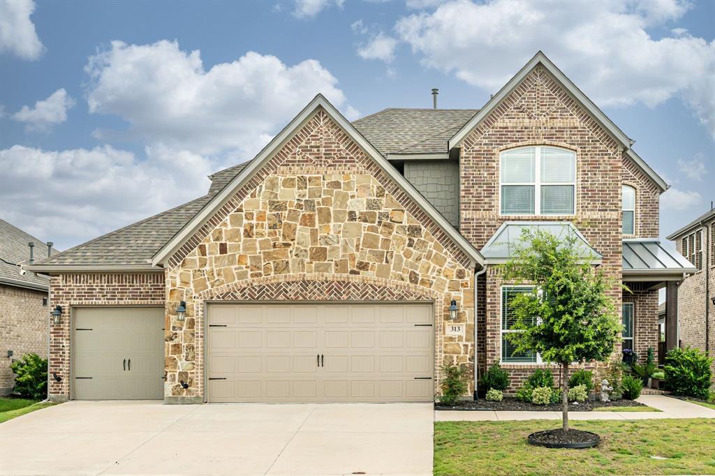 Exterior featuring a combination of brick and stone masonry, a two-car garage, established landscaping, and a covered entry porch