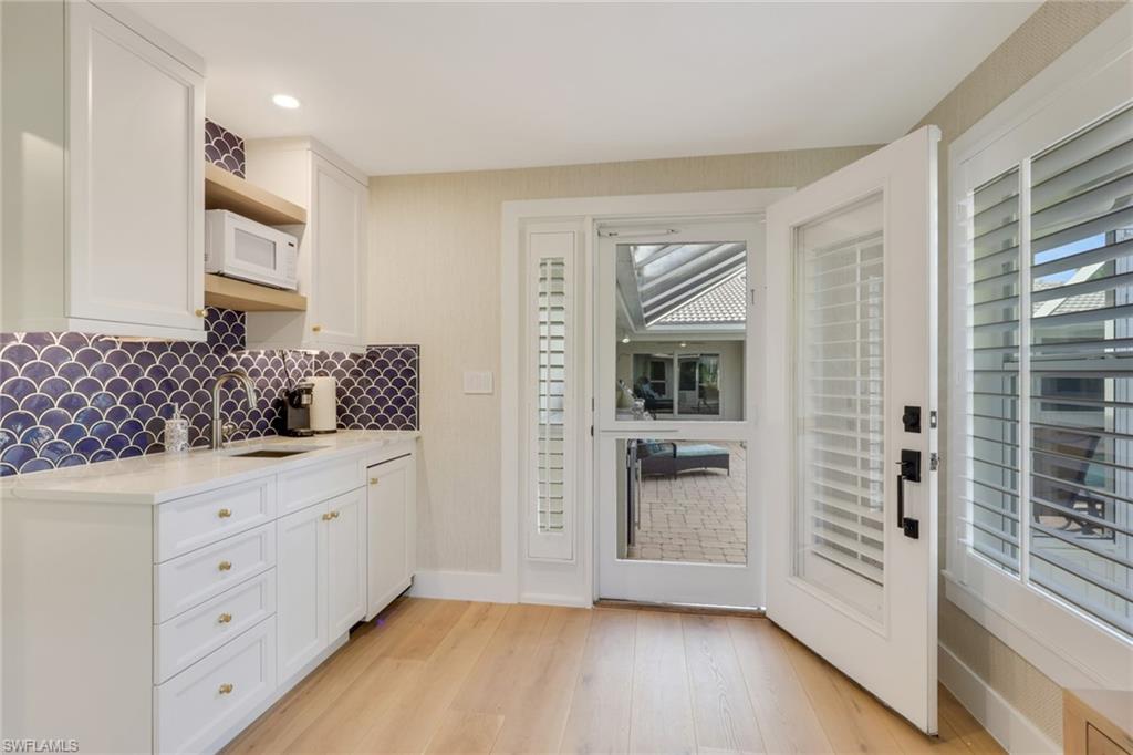 695 Regatta Road Naples, FL 34103 - Photo 18 of 43 Kitchen with white cabinets, light stone countertops, white microwave, tasteful backsplash, and light wood-type flooring