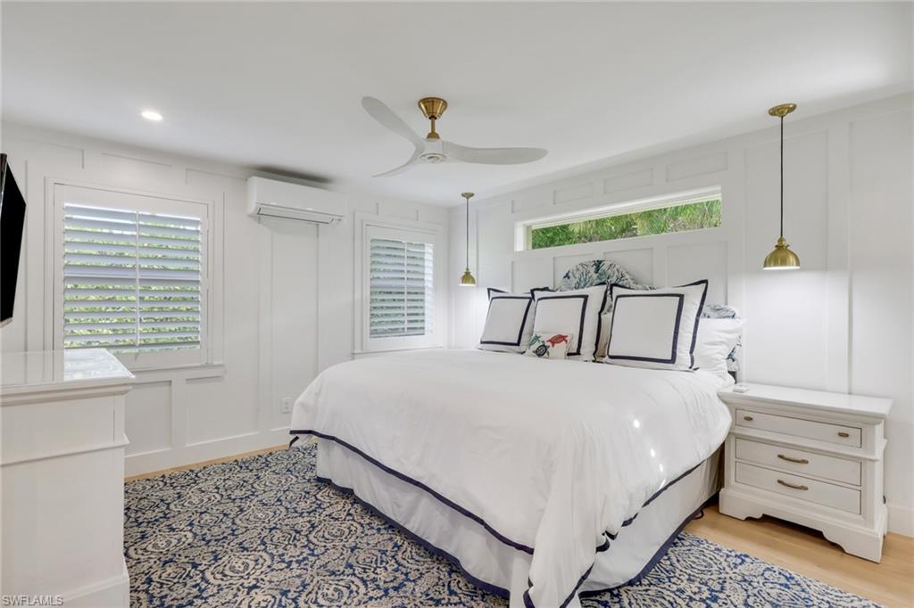 695 Regatta Road Naples, FL 34103 - Photo 22 of 43 Bedroom featuring a decorative wall, ceiling fan, multiple windows, a wall mounted AC, and light wood-style floors