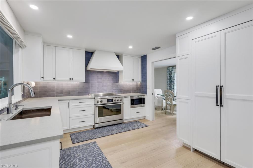 695 Regatta Road Naples, FL 34103 - Photo 6 of 43 Kitchen featuring stainless steel appliances, white cabinets, custom exhaust hood, light wood finished floors, and tasteful backsplash