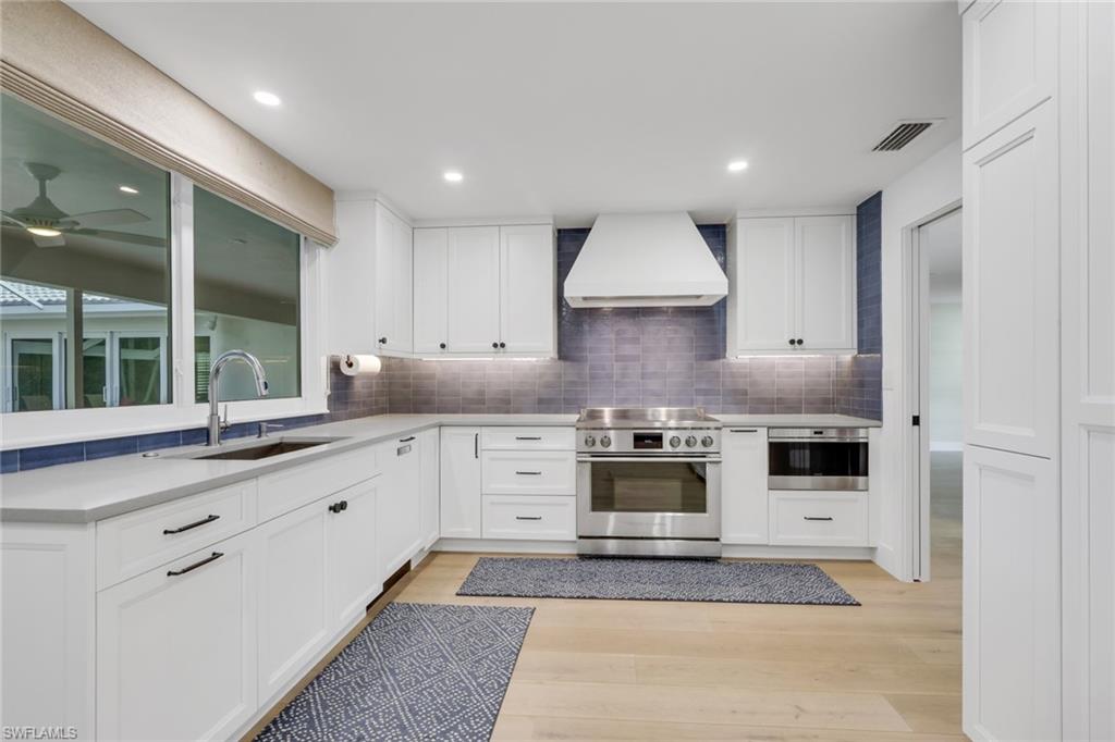 695 Regatta Road Naples, FL 34103 - Photo 7 of 43 Kitchen featuring white cabinets, custom range hood, stainless steel appliances, and light wood-style floors