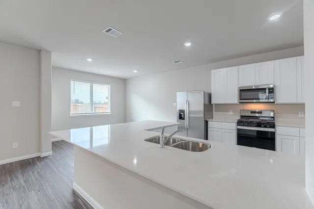 a kitchen with stainless steel appliances a sink a stove a microwave a sink a refrigerator with white cabinets and wooden floor