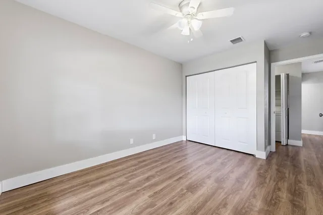 an empty room with wooden floor fan and windows