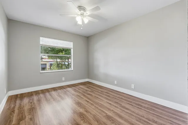 an empty room with wooden floor chandelier fan and windows