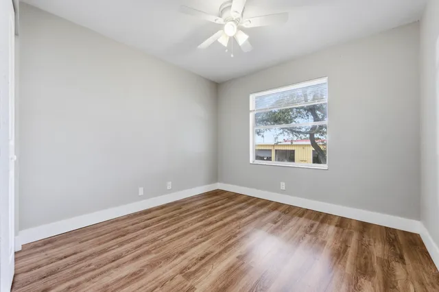 an empty room with wooden floor chandelier fan and windows